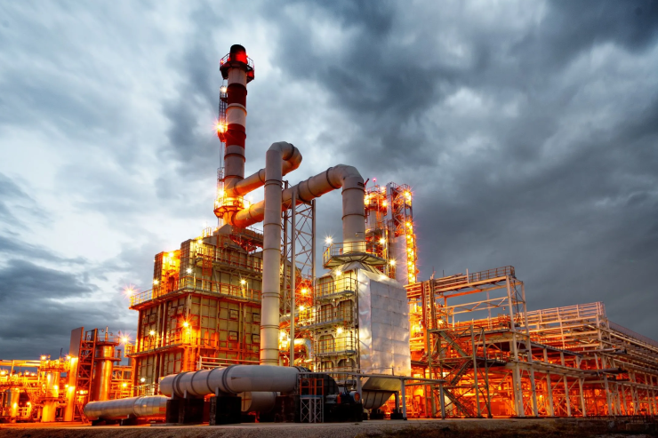 Industrial oil refinery plant at dusk with illuminated machinery and tall smokestacks