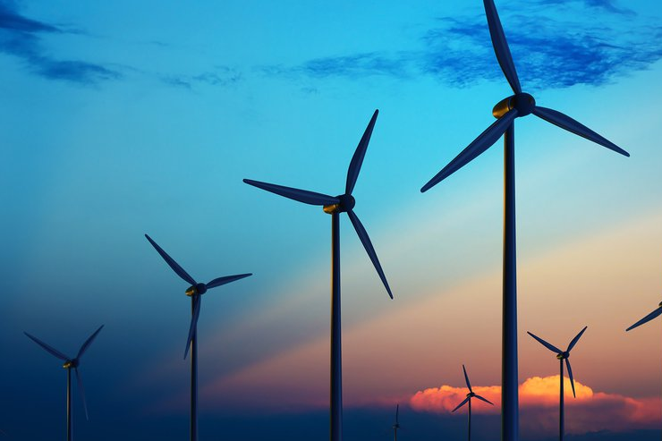 Wind turbines silhouetted against a vivid blue-orange sunset sky, symbolizing calm and clean energy.